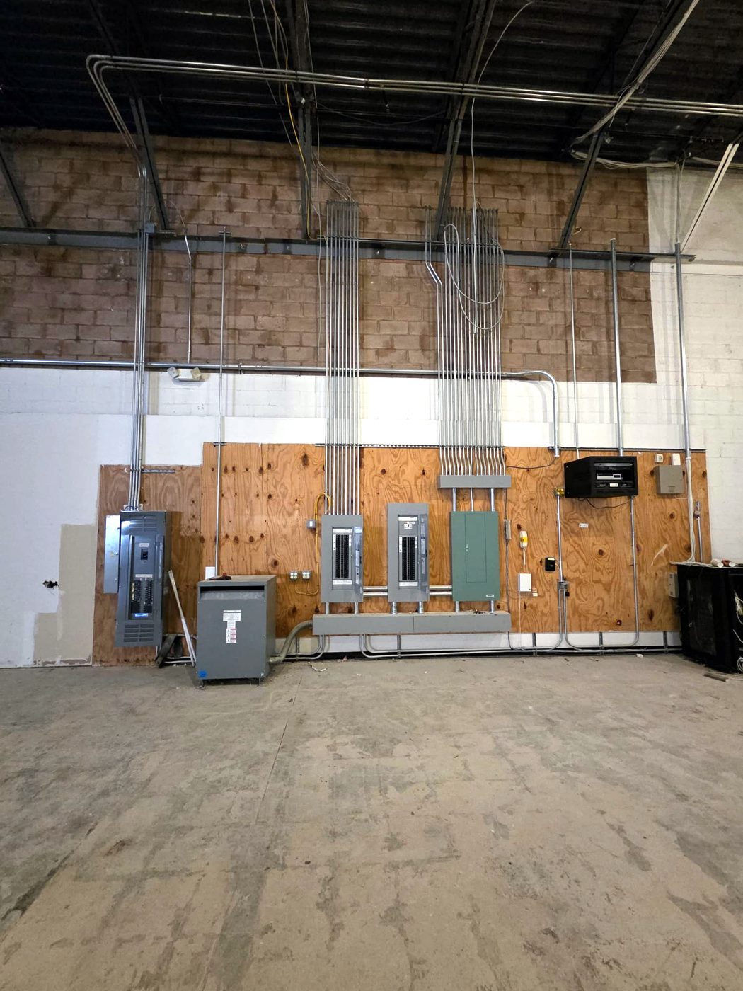 Warehouse wall with conduit risers feeding panels and a transformer