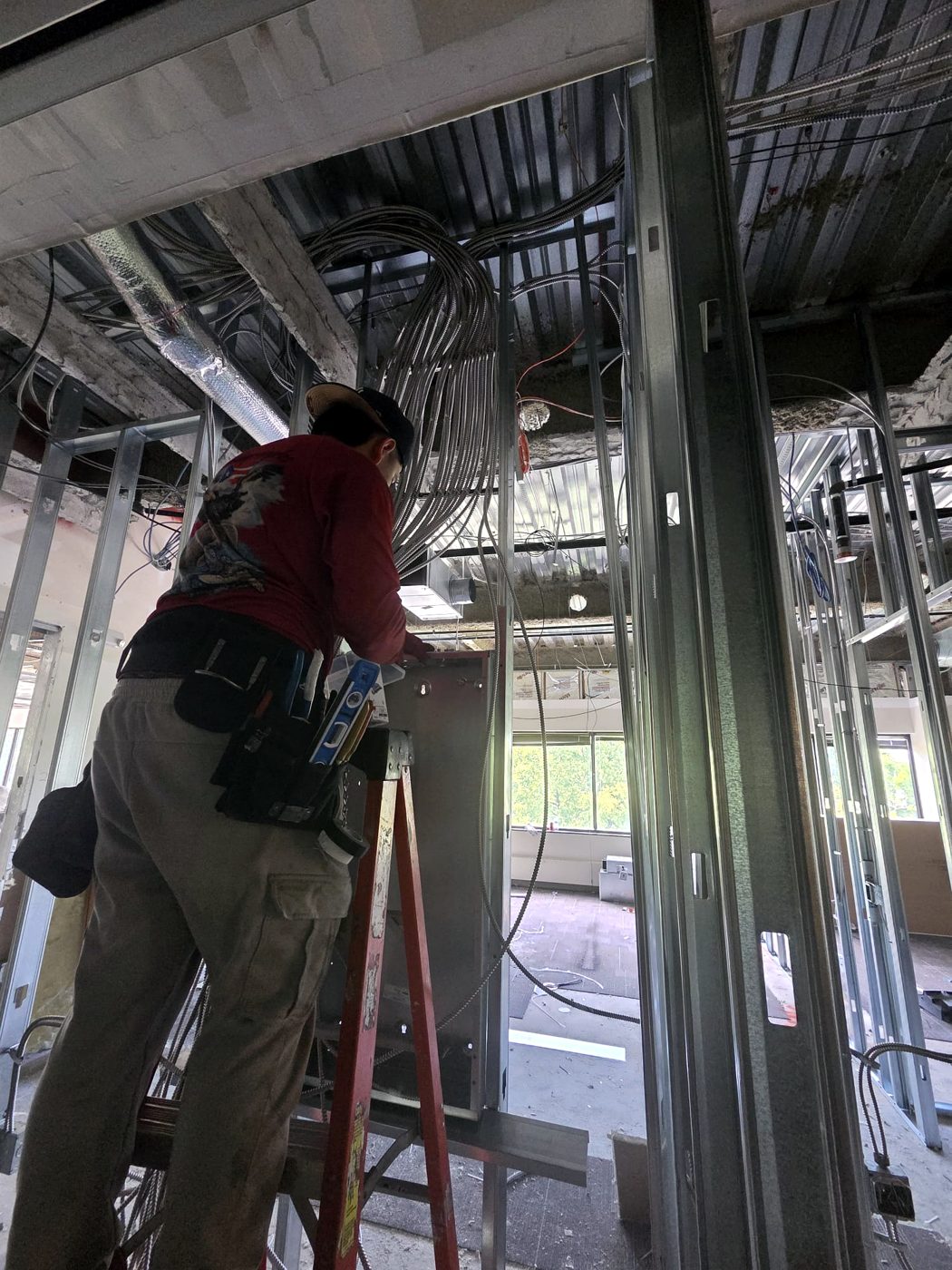 Electrician on a ladder pulling MC cable at a panel during build-out