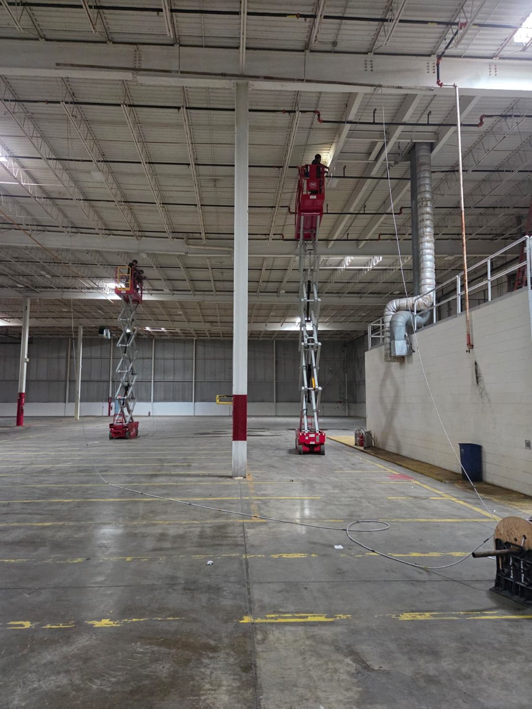 Large warehouse interior with two scissor lifts for overhead electrical work